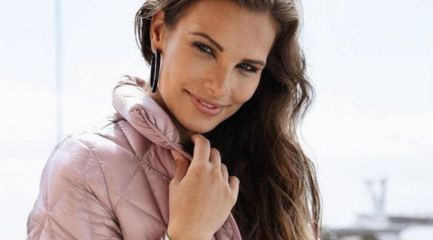 Kvinde iført en lyserød dunjakke fra Junge's Daisy-kollektion smiler til kameraet.