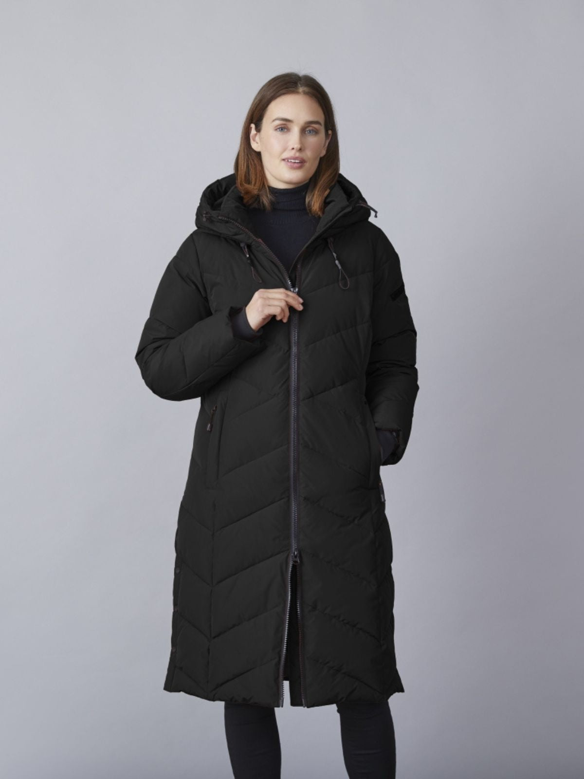 Model iført sort Katalin quiltet overgangsjakke til damer i lang comfort fit med hætte og lynlåslukning.