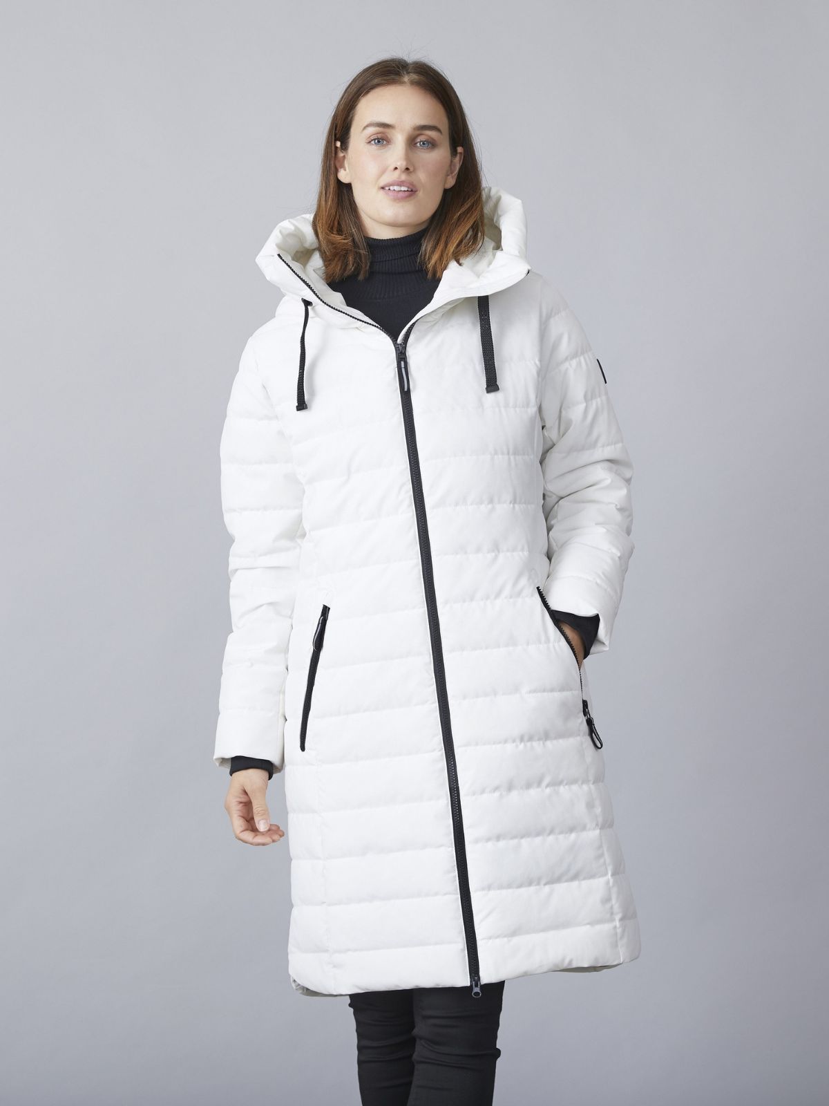 Model iført Kiki lang overgangsjakke til kvinder i winter white med hætte, lynlåslukning og quiltet design.