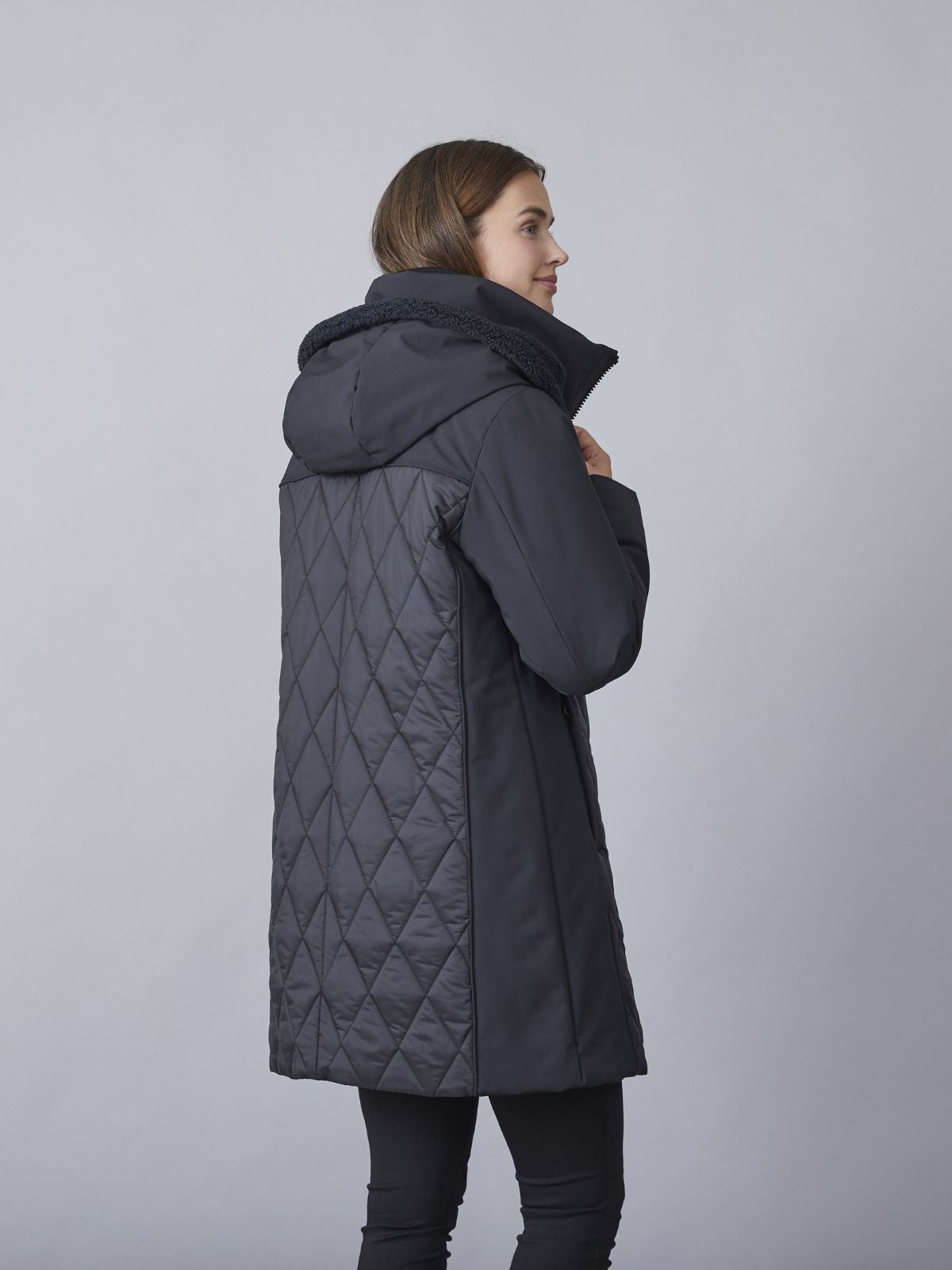 Model iført Kit overgangsjakke med hætte til damer i sort quiltet design med teddy-detaljer og comfort fit.
